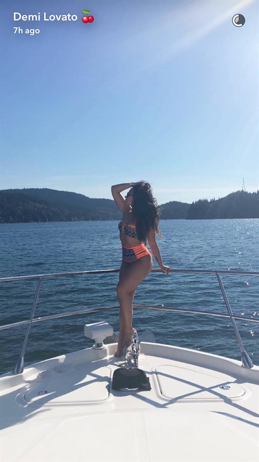 Demi Lovato showcasing her notorious Kardashian effect posturing in front of a boat in a hot neon bikini with a bold pattern and string cutouts.
